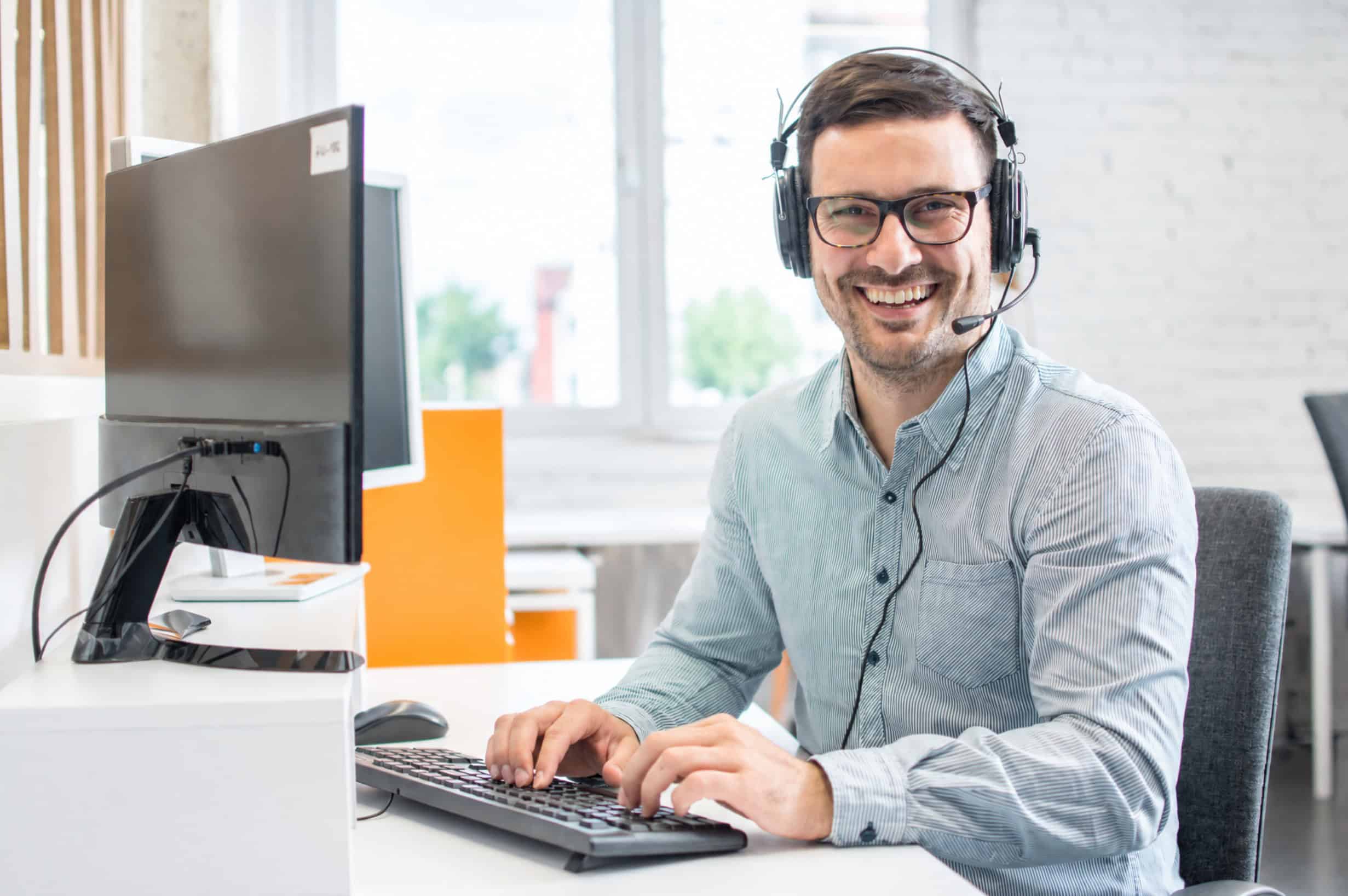 IT Technician Helpdesk Friendly IT support technician wearing headset at desk.